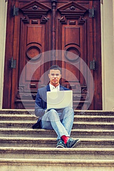Young man working on laptop computer, sitting on stairs  outside office building in New York City