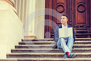 Young man working on laptop computer, sitting on stairs  outside office building in New York City