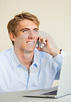 Young Man Working on Laptop Computer Talking on Phone