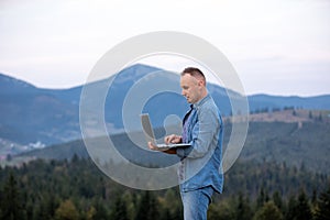 Young man working on laptop in the mountains. working online. Cellular network broaband coverage concept