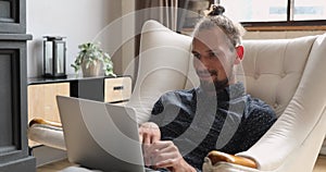 Young man working on laptop seated on comfy armchair