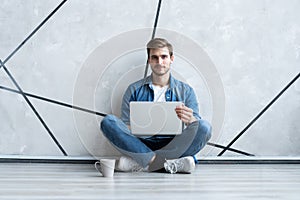 Young man working on laptop sitting on floor. Guy with computer reading news, surfing net or freelancing.