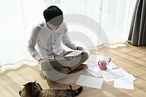 Young man working on a laptop and sitting on the floor in living room.