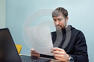 Young man working in the office with documents sitting at his desk. Business, training