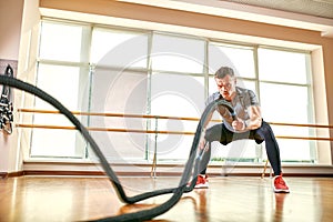 Young man working out with battle ropes at a gym