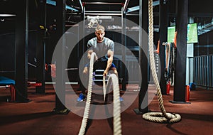 Young man working out with battle ropes at a gym