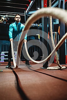 Young man working out with battle ropes at a gym