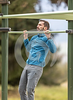 Young man working out calisthenics in an outdoor gym using parallel bars. He does push-ups on the bar. Concept of healthy