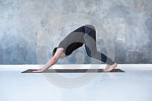 Young man working out, standing in yoga downward facing dog pose