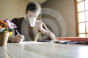 Young man working paperwork and bills at home and drinking coffee