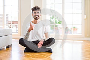 Young man working sitting casual on the floor at home doing happy thumbs up gesture with hand