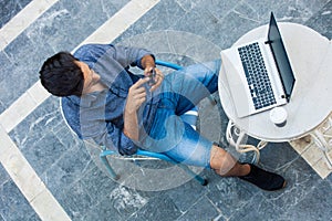 Young man working from terrace with laptop and smartphone