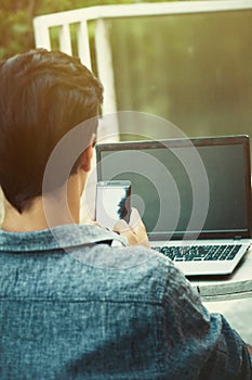 Young man working from terrace with smartphone and laptop