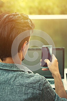 Young man working from terrace with smartphone and laptop