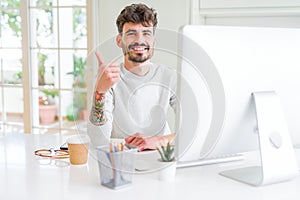 Young man working using computer happy with big smile doing ok sign, thumb up with fingers, excellent sign