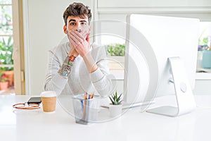 Young man working using computer shocked covering mouth with hands for mistake