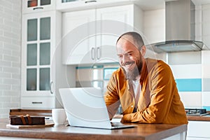 Young man working using laptop in kitchen in home interior. Smiling Freelancer works remotely from home. Happy man owner