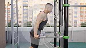 Young man workout out arms on dips horizontal bars training triceps and biceps doing push ups outdoors. Man in gym at
