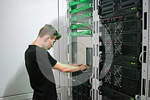 Young man works at a laptop near the racks with computer equipment. A teenager programmer programs server hardware in a modern