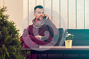 Young man works on the tablet computer while speaking on the phone in cafe - in urban public space