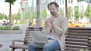 Young Man with Wrist Pain Using Laptop while Sitting on Bench