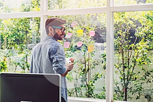 Young man writing  on the book while looking at sticky note paper