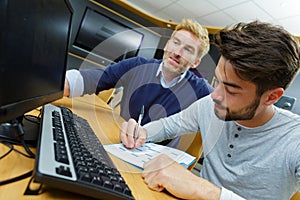 young man writing on note in front computer screen