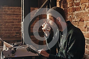 Young man writing on an old typewriter. In the meantime, he drinks coffee.