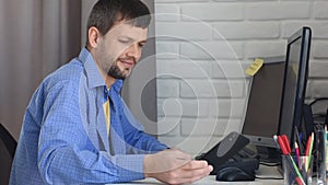 The young man wrote a message on the phone and continued to work on the computer