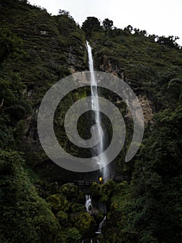 Young man in yellow jacket in front of El Chorro de Giron waterfall cascade cataract near Cuenca Azuay Ecuador photo