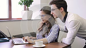 Young managers working in modern office, looking at laptop screen and talking.