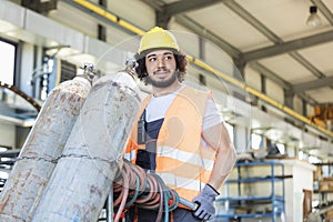 Young manual worker moving gas cylinders in metal industry