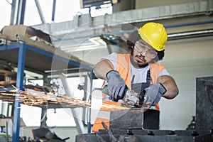 Young manual worker in protective workwear cutting metal in industry