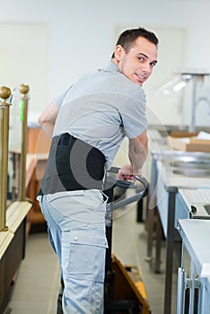 Young manual worker pushing pallet truck and wearing back support
