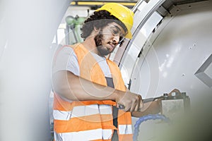 Young manual worker tightening bolts on machinery in factory