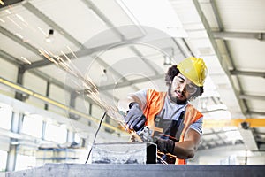 Young manual worker using grinder on metal in factory