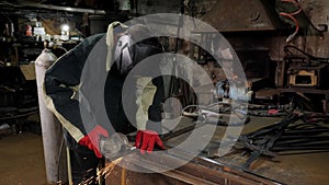 Young manual worker using grinder on metal in factory. Metal work.