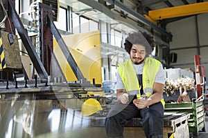 Young manual worker using mobile phone in metal industry