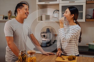 Young married couple cooking together in kitchen at home. Young woman feeding her man with kiwi and fruits indoor