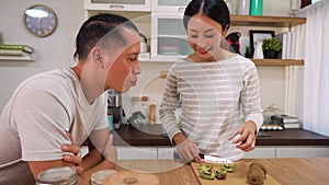 Young married couple cooking together in kitchen at home. Young woman feeding her man with kiwi and fruits indoors