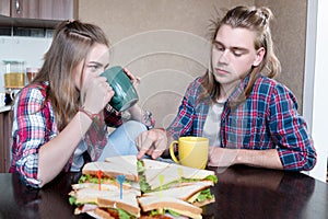 Young married couple man and woman are bored having breakfast in their kitchen. The girl drinks tea from a large mug and