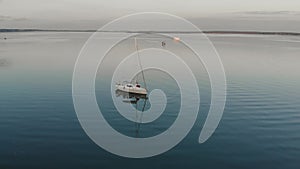 A young married couple in red pants sits on the bow of a white sailing yacht drifting on dark calm water