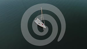 A young married couple in red pants sits on the bow of a white sailing yacht drifting on dark calm water