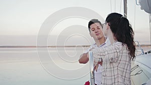 Young married couple in red pants sits on the side of a white sailing yacht sailing through dark calm water