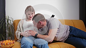 A young married couple is relaxing on the couch and watching TV. The baby is pushing in the stomach. Young family
