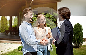 Young married couple shaking hands with realtor, making deal about house purchase outside