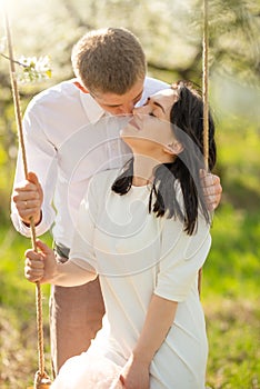 Young married couple, on a swing in a flowered garden or park. Warmly, love, spring and summer mood