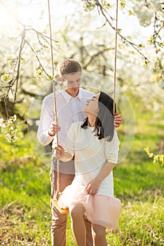 Young married couple, on a swing in a flowered garden or park. Warmly, love, spring and summer mood
