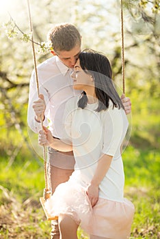 Young married couple, on a swing in a flowered garden or park. Warmly, love, spring and summer mood