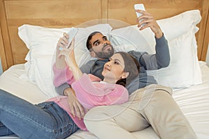 Young Married Couple Using Smartphones Lying In Bed At Home